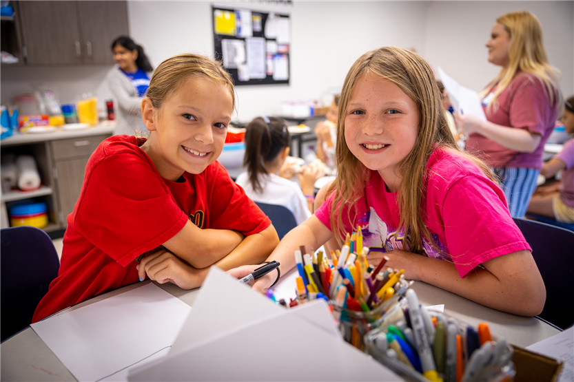 Two girls smile while sitting at a table